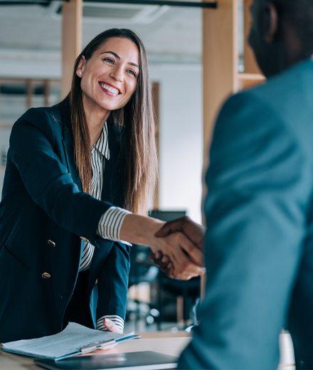 Woman shaking hands with man over desk.