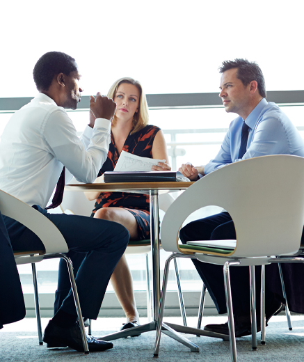 Image of 3 co-workers meeting around table at work.